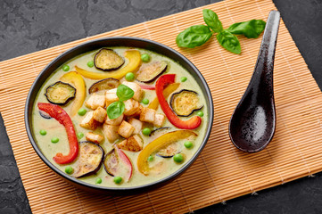 Vegetarian Thai Green Curry with tofu in black bowl at dark slate background. Veg Green Thai Curry is thailand cuisine dish with green chillies paste, basil, spices and vegetables. Thai Food