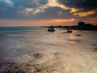 sunrise on the rocky beach in Andaman Islands, India. Sunlight is peeping through the clouds. Long exposure shot to create motion blur in the waves