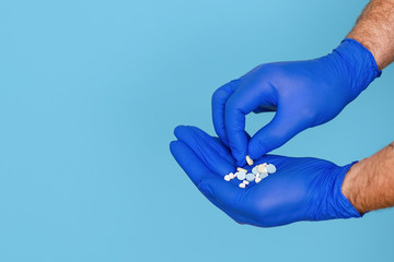 The pills are in the doctor's hands. Hands in blue medical gloves hold pills. Blue isolated background.