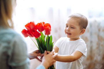 Little son congratulates mother and gives a bouquet of flowers tulips. Happy mother's day. Family holiday and togetherness.