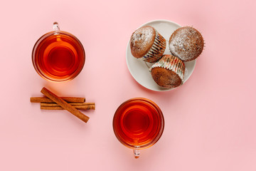 flat lay composition with two cups of tea and a dish with muffins on a pink background.