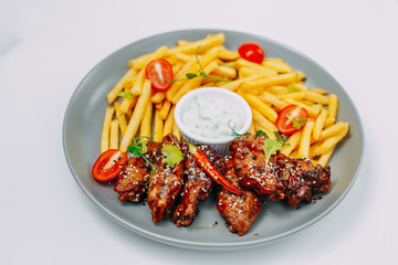 spicy chicken wings with french fries and sauce on an isolated white background