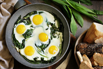 fried eggs with wild garlic as a shakshuka. fried eggs in a frying pan under gray marble on a table, top view. Keto diet dish
