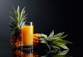 Pineapples and juice on a black reflective background.