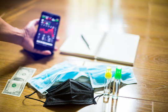 Black medicine mask with blurry red graph on smartphone, Dollar bill, wallet, alcohol spray and notebook. The concepts of the economic downturn from Covid 19.