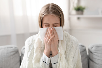 Young woman blowing her nose at home, close up portrait