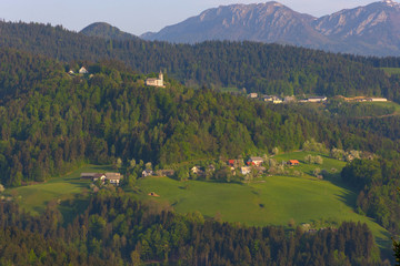 Fototapeta na wymiar Slovenian countryside in spring with charming little village and small white church on a hill, surrounded by Julian Alps mountains, in Slovenia