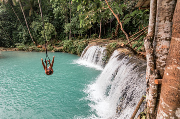 A young caucasian man plays with a rope swing over the Cambugahay Falls in Siquijor Island,...