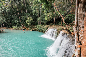 A young caucasian tattooed man plays with a rope swing over the Cambugahay Falls in Siquijor Island, Philippines © Daniel