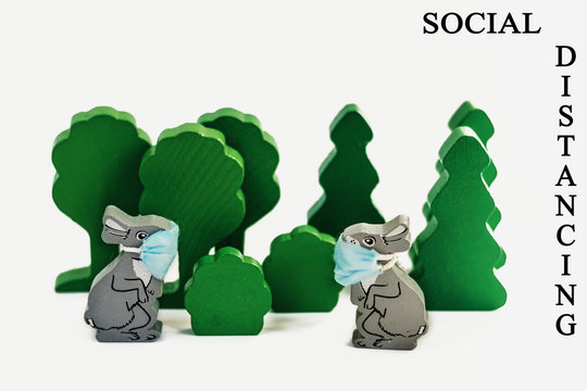 Wooden Easter bunnies in protective  masks at a distance from each other.The concept of social distance and quarantine during the outbreak of Covid-19.The inscription "SOCIAL DISTANCING"