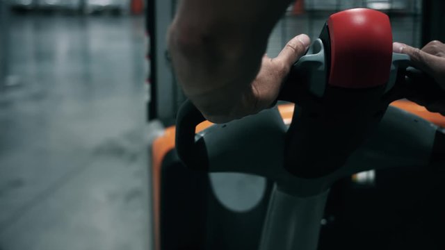 Close up of an operator who is on an electric pallet truck in a warehouse. We can see the hands of the operator who walks. Company and warehouse logistics