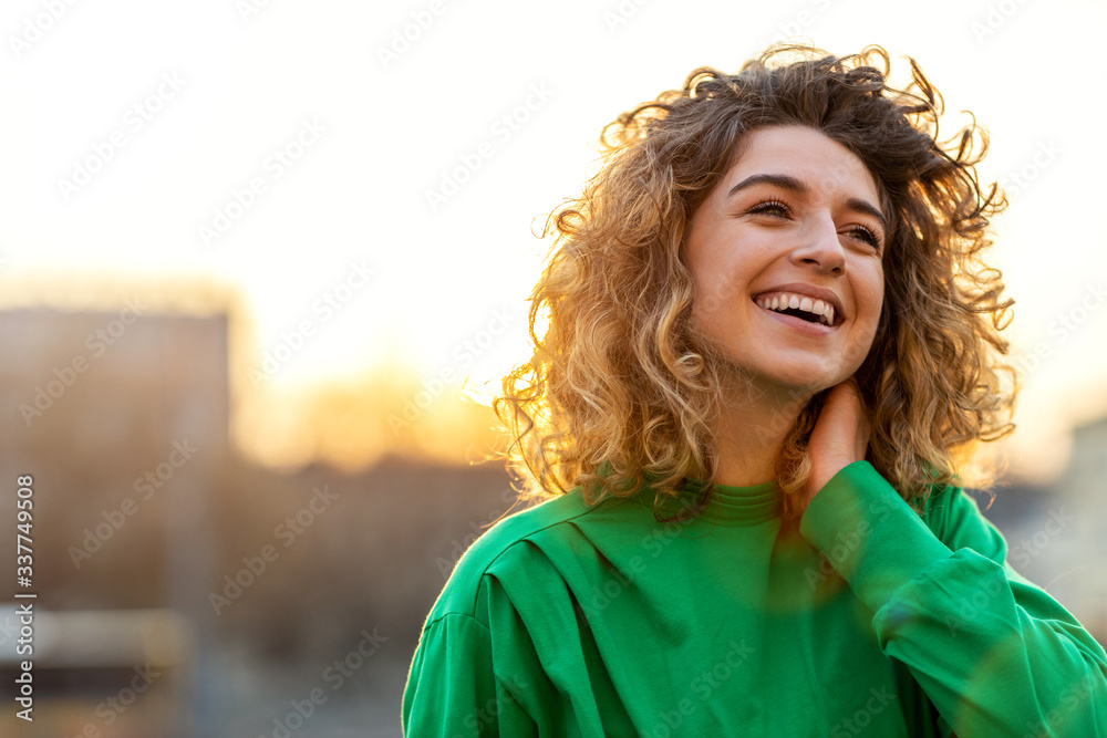 Wall mural portrait of young woman with curly hair in the city - Wall murals