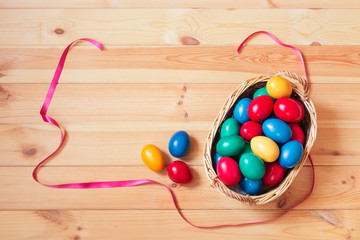 Colorful easter eggs in wicker basket and near on wooden table.
