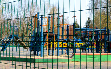 An empty playground across the metal fence, which is forbidden to visit during the quarantine period of the pandemic of COVID-19 disease caused by coronavirus