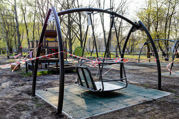 Fototapeta na wymiar An empty playground, wrapped with a warning red and white tape, which is forbidden to visit during the quarantine period of the pandemic of COVID-19 disease caused by coronavirus