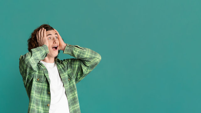 Excited millennial guy holding his head and shouting OMG on turquoise background, copy space