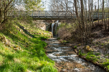 Fluss mit Wasserfall hinter Br&uuml;cke mit Eisengel&auml;nder