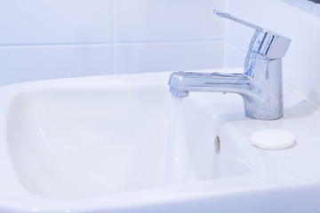 faucet water flows with soap on white basin in washroom interior