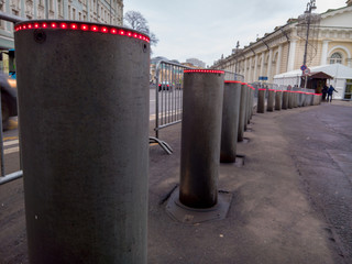 A long row of retractable metal bollards with hydraulic lift for traffic control, equipped with red LEDs on the upper end