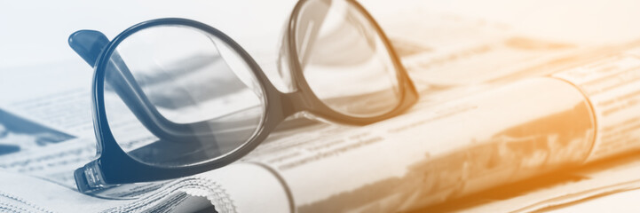 Media news concept, glasses for vision and a folded newspaper, close up. Panoramic image, toning