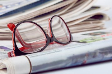 Media news concept, glasses for vision and a folded newspaper, close up.