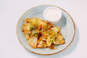Homemade fried potatoes with spices and sour cream on a white plate