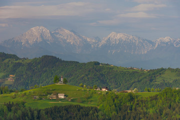 Fototapeta na wymiar Slovenian breathtaking landscape with Julian Alps and charming little church of Sveti Tomaz (Saint Thomas) on a hill. Beautiful spring in the mountains, in Slovenia.