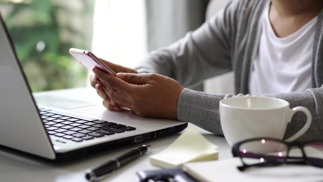 Young woman sitting at living room and working on laptop and smartphone at home