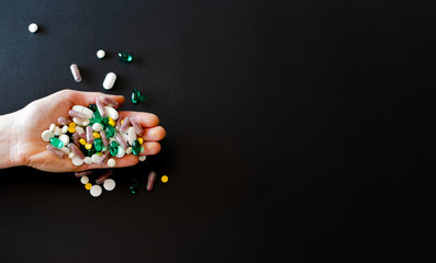 Lots of different medicine drugs, pills, tablets, capsules in woman hand on black matte background.  macro photo with selective focus. Medical pharmacy background. Copy space. Horizontal frame