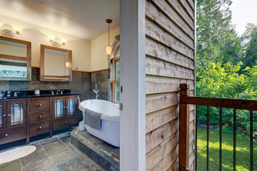 Bathroom interior with grey tiles and free standing white tub with open door to the balcony.
