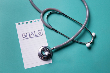 Stethoscope on color background New Year resolution Goals word as medical concept with blank paper and space for text .