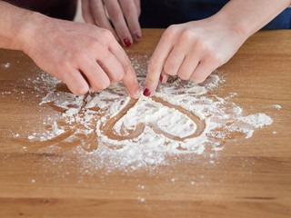 men's and women's hands draw a heart on a table covered with flour. baker's hand closeup.couple together Cooking pizza, bread during coronavirus