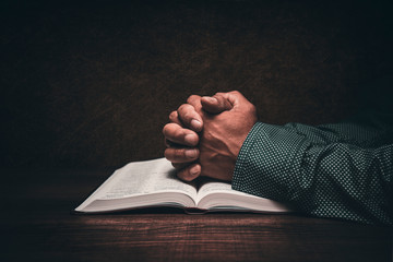 Hands of a man praying over an open bible - obrazy, fototapety, plakaty