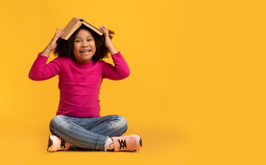 Portrait Of Playful Little Afro Girl With Opened Book On Head