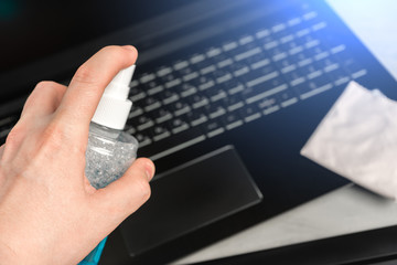A man's hand holds a bottle of liquid for cleaning equipment on the background of a laptop.