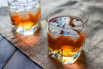 Two glasses of whiskey with ice cubes served on wooden planks.