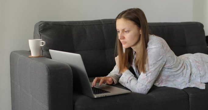 Serious young woman freelancer working on freelance from home typing email on laptop, focused girl using computer for study online at home on couch, female user busy on distance internet job.