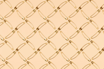 Safety pins pattern, bronze on a peach background.