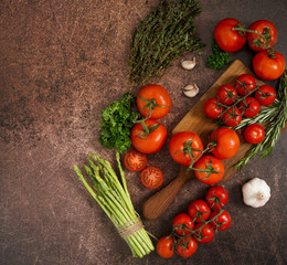 Red tomatoes, thyme, rosemary, garlic, parsley and asparagus on rustic rusty background