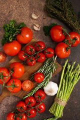 Red tomatoes, thyme, rosemary, garlic, parsley and asparagus on rustic rusty background