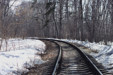 Fototapeta premium Railway passes through a spring forest, melting snow from the rays of the spring sun, sunny day, beautiful nature background.