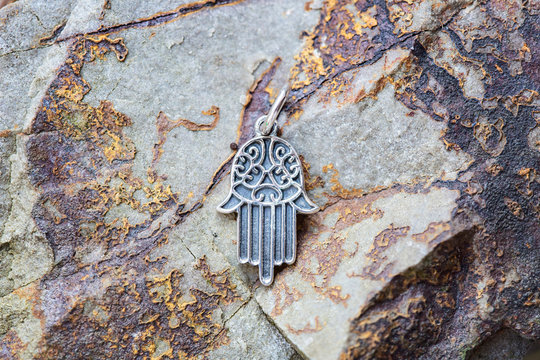 sterling silver metal pendant on natural background in the shape of hamsa, fatima hand