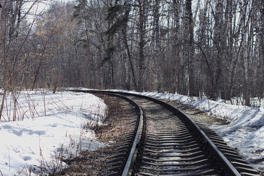 Railway passes through a spring forest, melting snow from the rays of the spring sun, sunny day, beautiful nature background.