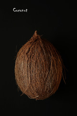 Close-up of an exotic and fresh coconut on a black background. Fresh, ripe and organic fruit of coconut. Bright brown nut full of vitamins. Healthy summer ingredients. Top view of a whole coconut