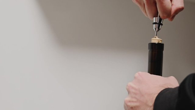 a man opens a bottle of wine with a metal corkscrew