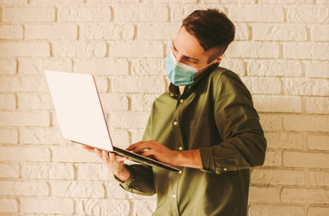 Man freelancer in protective face mask hold laptop in hand and talk cell phone. Business man in...
