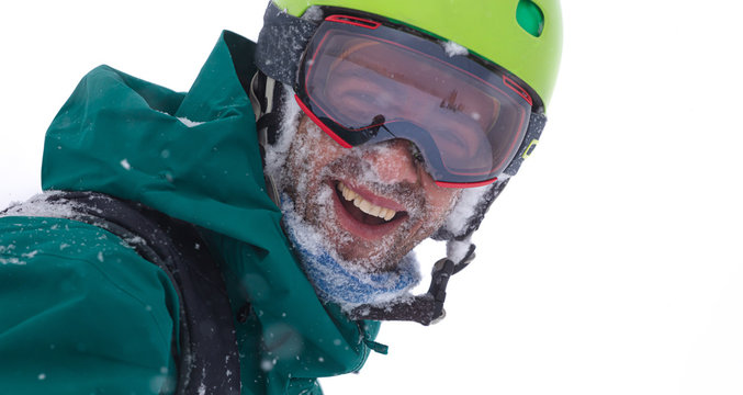 Skier's portrait during a big snowfall. the guy in the bright helmet and glasses at snow blizzard in the mountforest. Happy and smiling Freerider with snow on his face.