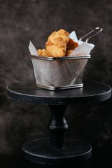 crispy chicken nuggets with golden crust in metal basket on black wooden table background