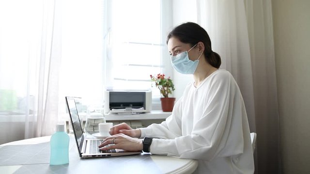 Coronavirus. Business woman working from home wearing protective medical mask. Girl in quarantine for coronavirus work at home office. Cleaning her hands with sanitizer gel.