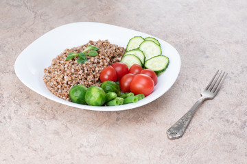 Tasty and healthy food from natural products. Salad of green vegetables, tomato and buckwheat in a white plate. Buckwheat with vegetables and eggs on a white plate.